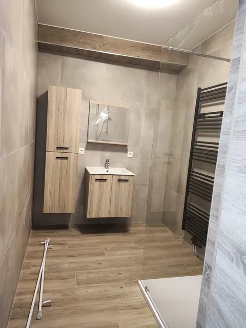 Salle de bain carrelée avec douche vitrée, meuble vasque et sèche-serviettes