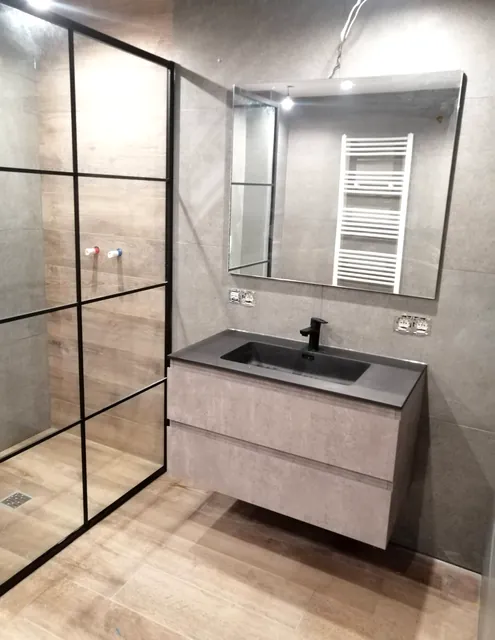 Salle de bain carrelée avec paroi de douche noire et meuble vasque